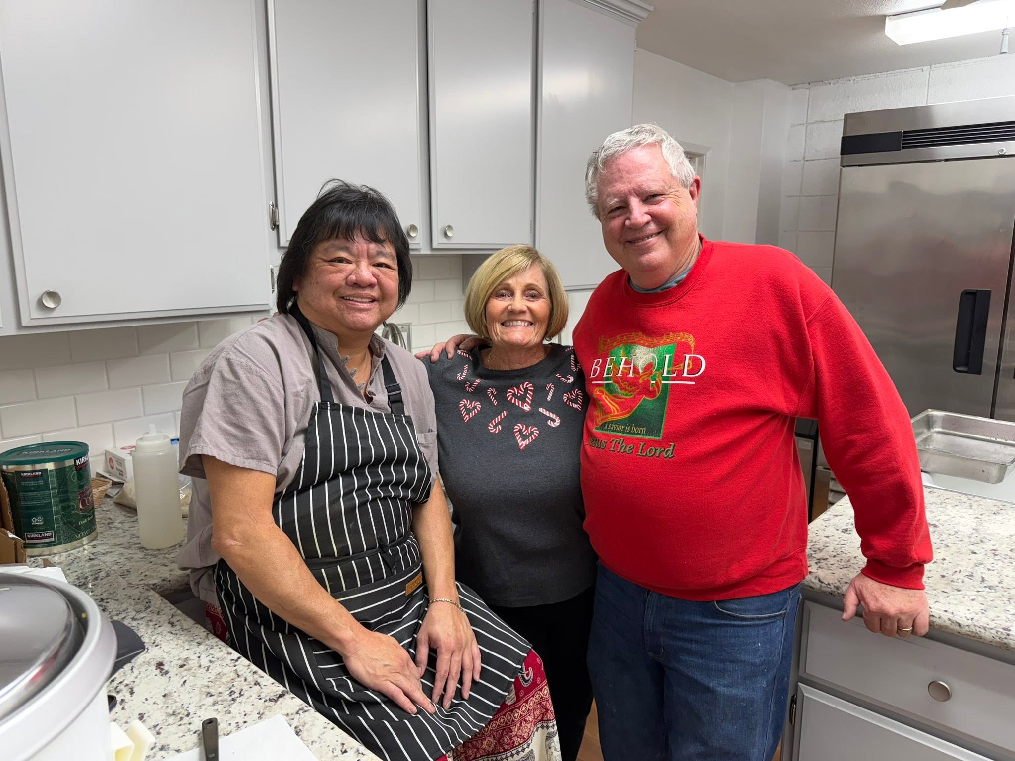 Three smiling church volunteers in the kitchen at the 2025 family Christmas dinner